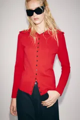 Chaqueta de punto color rojo, con cuello solapa y manga larga. Cierre frontal con fila de botones negros en contraste que se extienden también sobre el cuello.