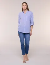 Camisa de corte clásico y silueta relajada con diseño de rayas verticales en blanco y negro. Presenta cuello camisero tradicional, cartera frontal con botones, un bolsillo aplicado en el pecho con rayas horizontales y mangas largas con sistema para arremangar.