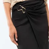 Falda larga de color negro con diseño cruzado y detalle de hebilla metálica dorada en la cintura. Presenta un corte midi con caída fluida y una abertura frontal.
