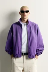 Cazadora relaxed fit de denim de algodón en color violeta, con efecto lavado, cuello alto, cierre frontal de cremallera y bolsillos en las costuras laterales. Presenta puños y dobladillo elásticos.