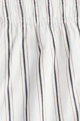 Pantalón tobillero de algodón blanco con rayas verticales finas en negro y beige. Presenta cintura elástica y corte amplio.