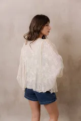 Kimono marfil de silueta amplia, confeccionado en tela con bordados florales y detalles calados. Cuenta con mangas amplias tres cuartos, frente abierto y terminaciones decorativas.