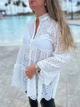 Camisa blanca de broderie con cuello mao, mangas largas amplias y cierre frontal con botones.