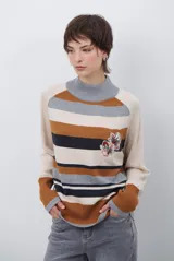 Polera de tejido de punto con diseño de rayas horizontales en tonos beige, marrón, gris y negro. Presenta cuello redondo y mangas largas con puños en contraste.
