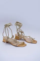 Sandalias doradas con tiras de cuerda para atar al tobillo.