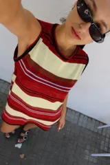 Vestido corto sin mangas, de tejido de punto a rayas horizontales en tonos rojo, crema, marrón y detalles en azul claro. Presenta bordes en negro y un calce amplio.