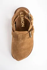 Zueco de gamuza color camel, con interior forrado en corderito, tira ajustable en el talón y suela de goma plana.