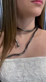 Gargantilla flexible en forma de serpiente de color gris oscuro metalizado, con diseño envolvente y cabeza detallada.