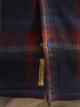 Sobrecamisa de tejido polar con estampado abstracto en tonos rojizos y azul marino. Presenta cuello clásico, cierre frontal con botones a presión, dos bolsillos frontales con solapa en el pecho y un parche decorativo.