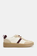 Zapatilla tipo bamba con diseño de paneles en combinación de colores y materiales, incluyendo detalles en cuero sintético y gamuza. Presenta suela de plataforma en contraste y cierre mediante cordones.