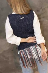 Musculosa tejida en punto calado color negro con destellos brillantes, presenta un diseño de flecos largos en el ruedo que combinan tonos rojizos, dorados y oscuros.