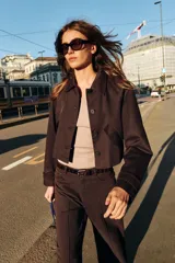 Chaqueta corta de color marrón oscuro, con cuello de solapa, manga larga con trabillas en los puños, bolsillos delanteros con solapa y cierre frontal con botones.