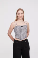 Top corto de escote cuadrado con breteles finos ajustables, confeccionado en tela con estampado de cuadros vichy en blanco y negro. Presenta un pequeño lazo decorativo en el centro del escote y un corte estilo corset con ruedo en punta.