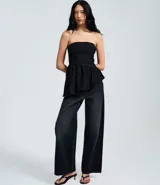 Blusa peplum sin tirantes de color negro, confeccionada en bengalina con diseño asimétrico en el dobladillo.