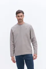 Remera de manga larga tipo henley, confeccionada en algodón con textura, color gris claro. Presenta una cartera frontal con botones y un pequeño logo bordado en el pecho.