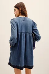 Vestido corto de tencel en color azul, con mangas largas abullonadas y escote en V profundo. Cuenta con detalles de bordados oscuros en el pecho, los puños y el ruedo, y una falda de corte evasé.
