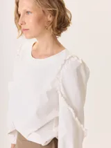 Camisa de color marrón con diseño combinado, presentando mangas abullonadas con volados en los hombros y cuerpo de algodón. Combina una textura de tela de camisa en mangas y delantero con una espalda de tejido elástico.