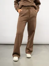 Pantalón de corte recto confeccionado en felpa, con cintura elástica ajustable mediante cordón y bolsillos laterales. Presenta un diseño minimalista con el logo de la marca sutilmente bordado en la parte frontal.