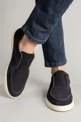 Botineta masculina de gamuza en color azul marino, con diseño slip-on sin cordones y suela de goma blanca. Presenta costuras visibles en la puntera y un estilo urbano minimalista.
