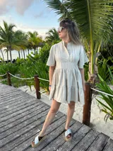 Vestido corto color beige de lino, con cuello mao, mangas cortas con volados, tablas en el canesú y falda escalonada con volantes.