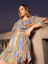 Conjunto de dos piezas compuesto por un top corto de mangas abullonadas con elástico y una falda corta con volados, ambos confeccionados en tela estampada a rayas multicolores.