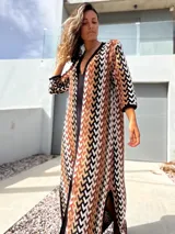 Vestido largo de tejido de punto con diseño geométrico en tonos tierra, negro y blanco. Presenta escote en V profundo, mangas tres cuartos y tajos laterales en la falda.