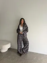 Conjunto de camisa y pantalón de viyela a cuadros en tonos marrón, blanco y azul. La camisa es oversize de manga larga con bolsillos frontales y cierre de botones. El pantalón es recto y holgado.