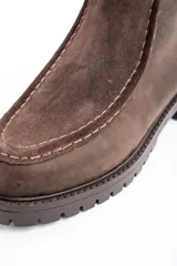 Bota corta de cuero vacuno en tono marrón oscuro, con diseño de costuras visibles en el empeine y suela de goma dentada tipo track.