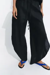 Pantalón de tiro medio confeccionado en lino, con cintura elástica ajustable mediante cordones. Presenta un diseño de pierna ancha con bajo redondeado y aberturas laterales.