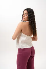 Chaleco de escote en V con silueta entallada y cierre frontal de botones, confeccionado en tela tipo nylon amasado de color manteca con textura y sutil brillo.
