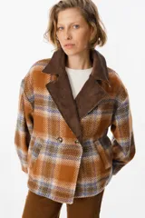 Blazer de corte holgado con diseño a cuadros en tonos naranja, azul y marrón. Presenta solapas anchas de pana en color marrón oscuro, cierre frontal cruzado con dos botones y bolsillos laterales integrados.