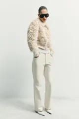 Chaqueta tipo bomber de textura afelpada en color crema, con cuello solapa, cierre frontal con cremallera y puños y cintura de tejido elástico acanalado.