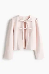 Chaqueta rosa claro de tejido grueso, con escote redondo, frente abierto con cierre de tiras dobles para anudar, hombros fruncidos y mangas largas.