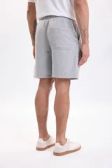 Bermuda de felpa de algodón gris melange con cintura elástica ajustable mediante cordón y bolsillos laterales.