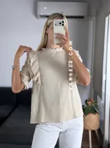 Blusa de símil lino color beige, con cuello redondo fruncido, doble volado en los hombros con detalle de encaje y manga 3/4.