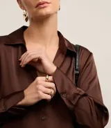 Camisa de satén color verde lima, con cuello inglés, cierre frontal con botones y mangas largas con puños abotonados. Presenta un acabado brillante y fluido.