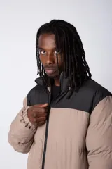 Campera puffer de diseño bicolor, con cuerpo en tono beige y canesú superior en color negro. Presenta cuello alto, cierre frontal completo y puños elásticos.