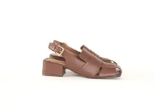 Sandalia de cuero marrón con tiras anchas entrecruzadas en la parte delantera, punta cuadrada y talón abierto con pulsera ajustable y hebilla metálica dorada. Cuenta con un taco ancho de 4 cm forrado en cuero.