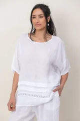 Blusa de lino color blanco, de corte amplio, con escote redondo, mangas cortas y detalle de guarda calada horizontal en la parte inferior.