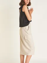 Falda midi color beige, de tiro alto con elástico en la cintura trasera, cierre y botón delantero. Tiene bolsillos delanteros y bolsillos cargo a los costados, con tajo en el delantero.