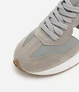 Championes estilo jogging con diseño de paneles en tonos gris, blanco y negro. Presentan cierre por cordones, suela de goma con relieve que se extiende hacia el talón y acabado en poliuretano.