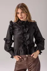 Camisa negra de corte entallado con volados decorativos en el cuello, la botonadura frontal, los hombros y las mangas. Presenta mangas largas con puños ajustados y un ruedo con volado inferior.