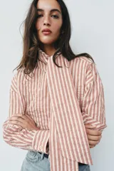 Camisa de rayas rojas y blancas, cuello redondo con lazada integrada y manga larga.