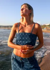 Top corto de denim azul con estampado de monogramas, escote recto, breteles finos y cierre en la espalda.