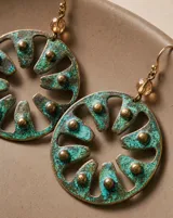 Aros colgantes de diseño circular con calados radiales y acabado en pátina de cobre oxidado, con detalles de tachas metálicas. Cuentan con pasante de plata esterlina.