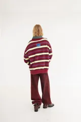 Sweater de textura peluda con diseño de rayas horizontales en tonos bordó, amarillo y azul. Presenta un corte holgado, cuello redondo y un pequeño logo bordado en el centro del pecho.