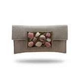 Bolso tipo sobre color dorado, confeccionado en yute de algodón con acabado texturizado y un llamativo aplique central metálico rectangular con piedras de resina en tonos tierra y gris. Incluye asa de cadena para llevar al hombro.