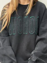 Buzo oversize de color negro con calce relajado y mangas amplias. Presenta letras en relieve con bordes desflecados en el frente y un ruedo inferior también desflecado.