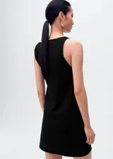 Vestido corto negro sin mangas, confeccionado en punto fino, con cuello barco y tirantes asimétricos.