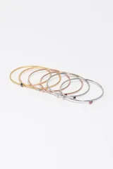 Set de pulseras rígidas de metal en tonos plateado, dorado y rosé, cada una con un pequeño cristal de color incrustado.